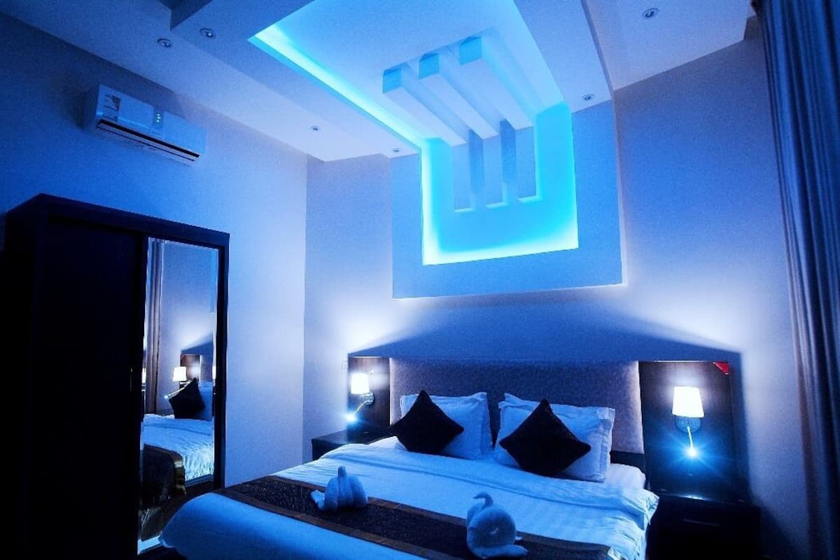 Ein modernes Hotelzimmer mit einem großen Bett, Nachttischlampen, einer Deckenleuchte und einem Spiegel.