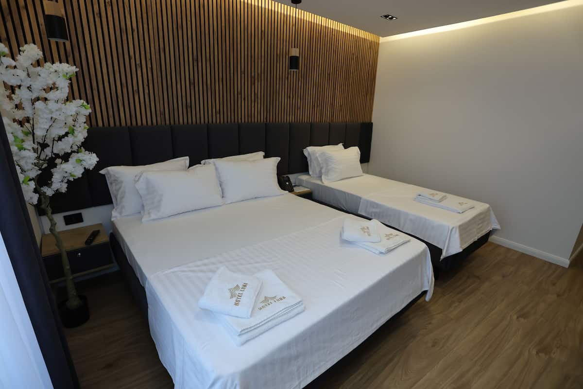 A hotel room with two beds, wooden paneling on the wall, a nightstand with a lamp, and a potted plant.