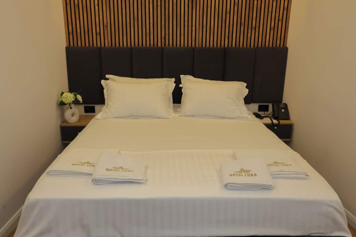 A hotel room with a large bed, two pillows, a nightstand with a phone, and a vase with flowers.