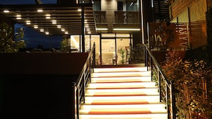L’entrée d’un hôtel, avec un tapis rouge et des marches menant aux portes, sur lesquelles on peut lire l’inscription « HÔTEL LUNA ».