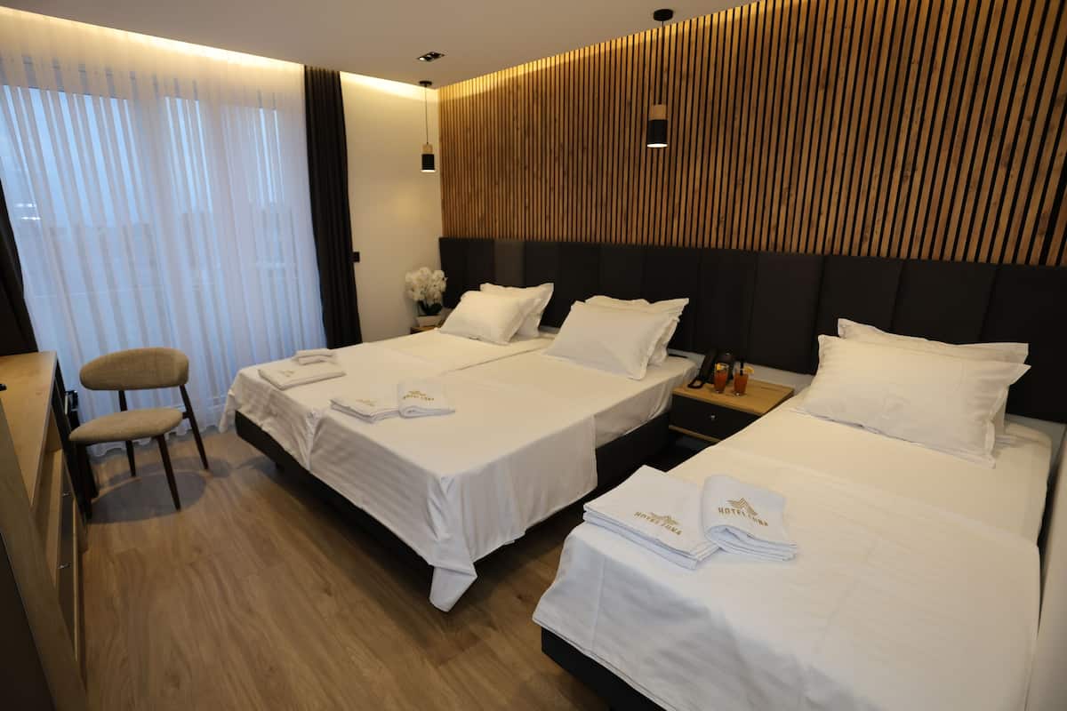 A hotel room with two beds, a wooden headboard, a desk with a chair, and a small table with a vase of flowers.