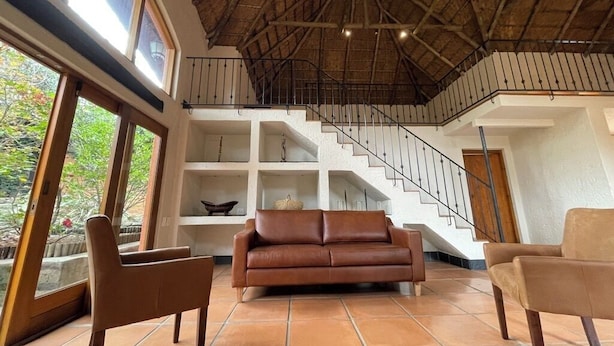 A spacious living area with a brown leather sofa, two armchairs, and a staircase leading to an upper level.