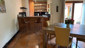 A compact kitchen with a dining area, including a wooden table, chairs, and a small bar area with stools.
