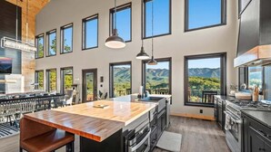 A modern kitchen with a large island, multiple windows, and a view of mountains. - Luxury Smoky Mtn Cabin | Infinity Pool & Views (Cosby)