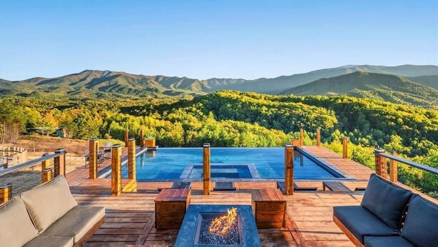A wooden deck with a pool, seating, and a fire pit, overlooking a mountainous landscape. - Luxury Smoky Mtn Cabin | Infinity Pool & Views (Cosby)