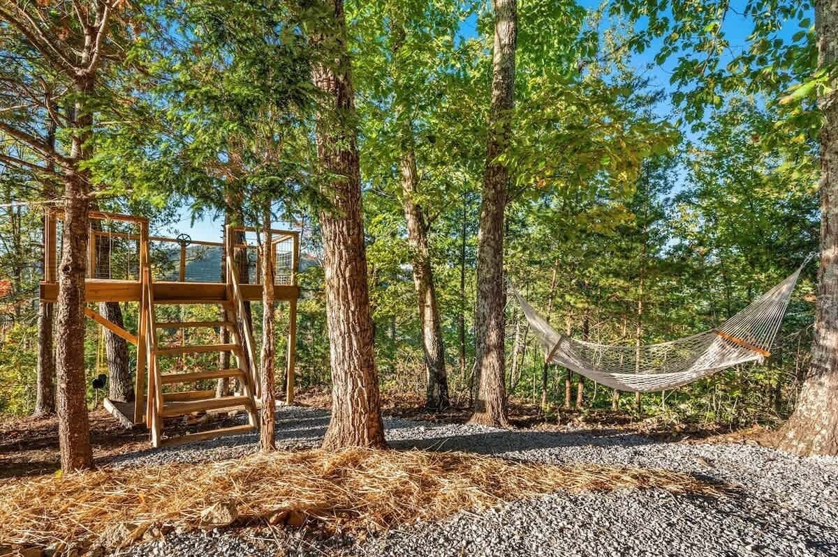 A hammock between trees, a wooden structure, and a gravel path.