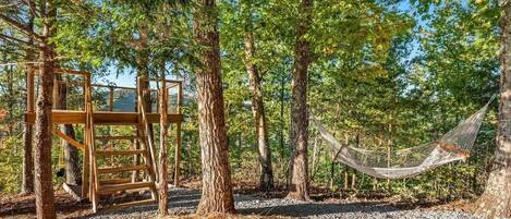 A hammock between trees, a wooden structure, and a gravel path.