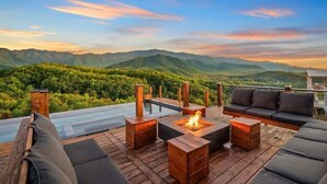 A deck with outdoor furniture, a fire pit, and a pool overlooking a mountainous landscape. - Luxury Smoky Mtn Cabin | Infinity Pool & Views (Cosby)