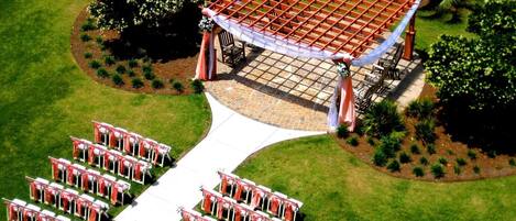 An outdoor wedding ceremony setup with a covered seating area and a white aisle leading to a stage.