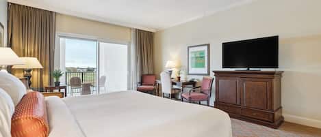 A hotel room with a large bed, a desk with a chair, a television, and a balcony with curtains.