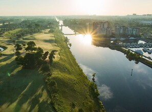 A golf course adjacent to a body of water with a bridge and buildings in the background. - Marina Inn Grande Dunes Condos & Suites (Myrtle Beach)