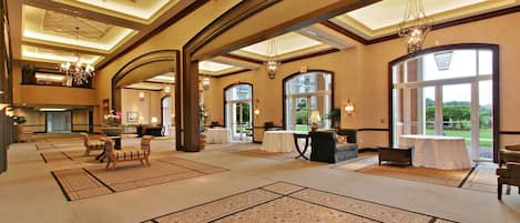 A spacious lobby with high ceilings, chandeliers, and large windows offering views of the outdoors.
