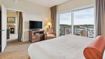A hotel room with a large bed, a television, a desk with a lamp, a chair, and a balcony with a view of the outdoors.