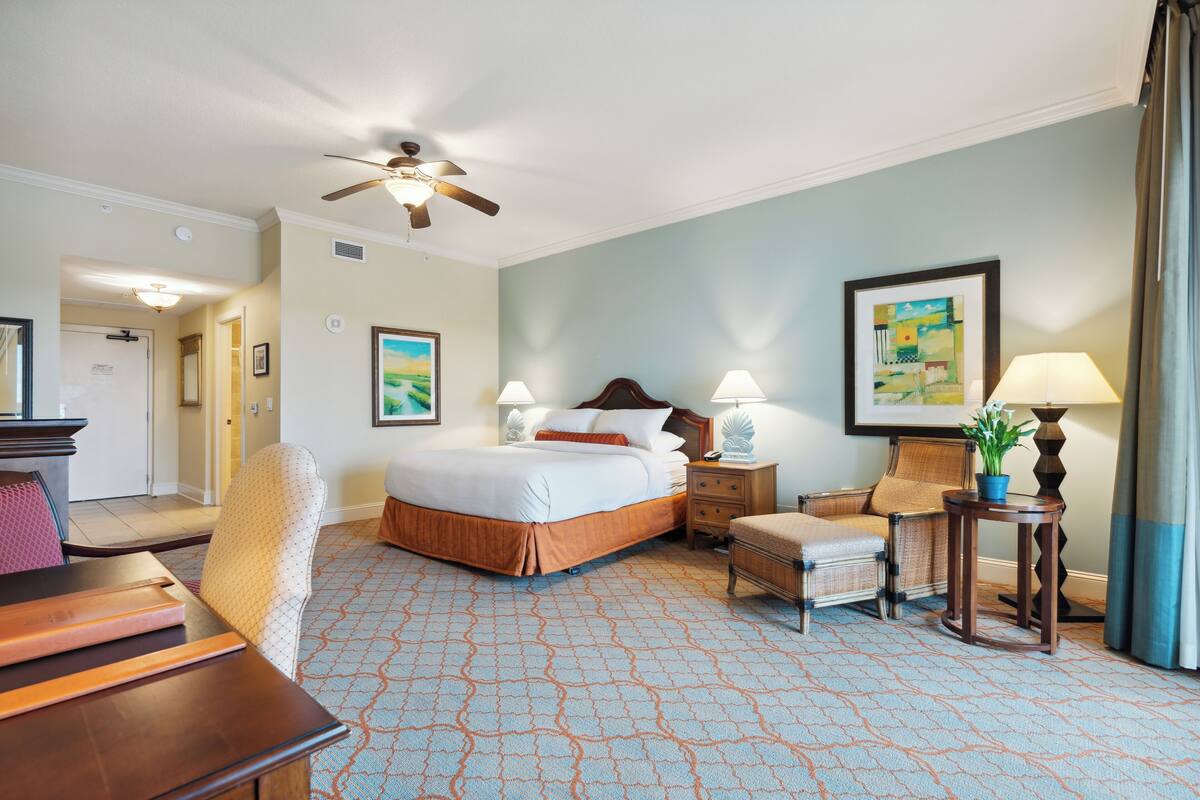 A hotel room with a bed, two bedside tables, a chair, a desk, and a ceiling fan.
