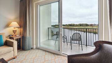 A hotel room with a balcony, a sofa, a table with a lamp, and a view of a golf course.