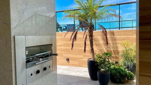 A modern outdoor kitchen area with a built-in grill, potted plants, and a view of the ocean. - Green Porto 104  (Ipojuca)