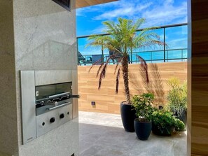 Un espace cuisine extérieur moderne, doté d’un barbecue encastré, de plantes en pot et offrant une vue sur l’océan.