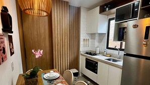 A modern kitchen with a dining table set for two, a microwave, stove, and refrigerator. - Green Porto 104  (Ipojuca)