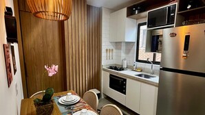 A modern kitchen with white cabinets, a stainless steel refrigerator, a microwave, and a dining area with a wooden table set for two. - Green Porto 104  (Ipojuca)