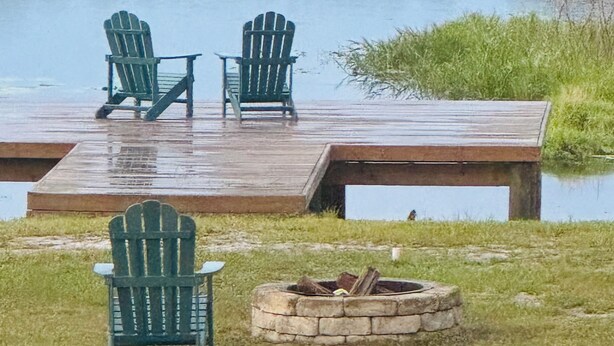 Une jetée en bois avec deux fauteuils Adirondack et un foyer en pierre.