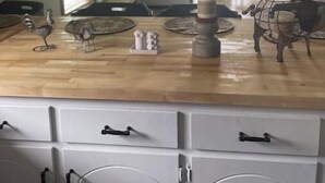 Une cuisine avec un plan de travail en bois, des armoires blanches et un coin repas à l’arrière-plan.