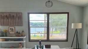 Un salon avec un canapé gris, une table agrémentée d’objets décoratifs, une grande fenêtre donnant sur un lac et un lampadaire.
