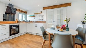 Een moderne keuken met witte kasten, een ingebouwde oven en een houten aanrecht. Er staat een eettafel met stoelen en een vaas bloemen.