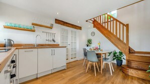 Een moderne keuken met witte kasten, een houten aanrecht en een eethoek met een tafel en stoelen. Een houten trap leidt naar een hoger gelegen verdieping.