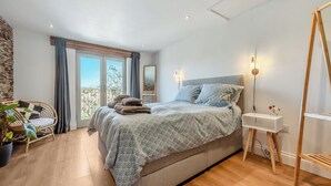 Een slaapkamer met een bed, een stoel, een nachtkastje en een raam.