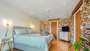 Een slaapkamer met een bed, nachtkastje, televisie en een stenen muur.