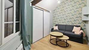 Ett rum med en mörkgrå soffa, två kuddar, ett runt träbord och en mönstrad tapet.