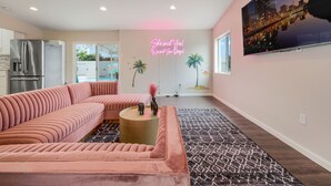 A modern living room with a pink sectional sofa, a round coffee table, and a neon sign on the wall. - Girls  & Family Trip+Pool+beauty bar, San Diego (La Mesa)