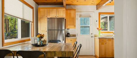 A modern kitchen with wooden cabinets, a stainless steel refrigerator, and a dining table with chairs.