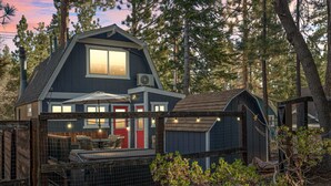 A two-story cabin with a large window, outdoor seating area, and a fenced garden. - National Forest View Chalet: Hot Tub, A/C & BBQ (Big Bear Lake)