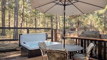 Een terras met jacuzzi, tuinmeubilair en een houten omheining met uitzicht op een bos.