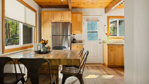 A modern kitchen with wooden cabinets, a stainless steel refrigerator, and a dining table with chairs. - National Forest View Chalet: Hot Tub, A/C & BBQ (Big Bear Lake)