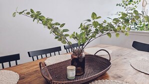 A dining table with a woven tray, a glass vase with a plant, and a candle.