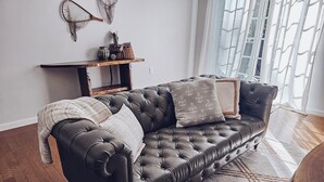 A dark brown leather sofa with tufted detailing, a patterned throw blanket, and two pillows with floral designs. A wooden side table with decorative items is positioned against the wall.
