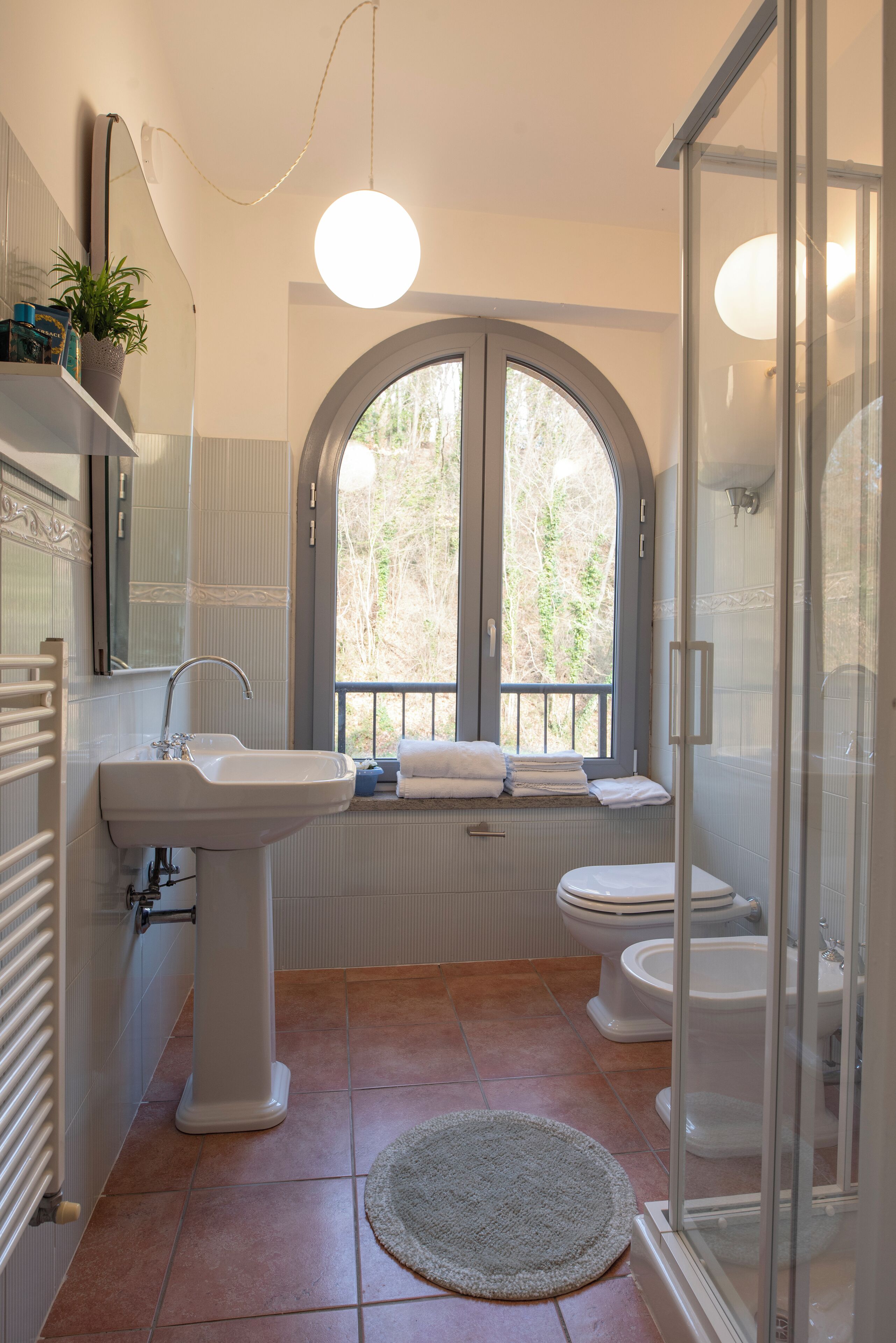 Ein Badezimmer mit Waschbecken, Toilette und Dusche. Ein Fenster bietet Blick auf Bäume.