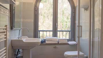 Ein Badezimmer mit Waschbecken, Toilette und Dusche. Ein Fenster bietet Blick auf Bäume.
