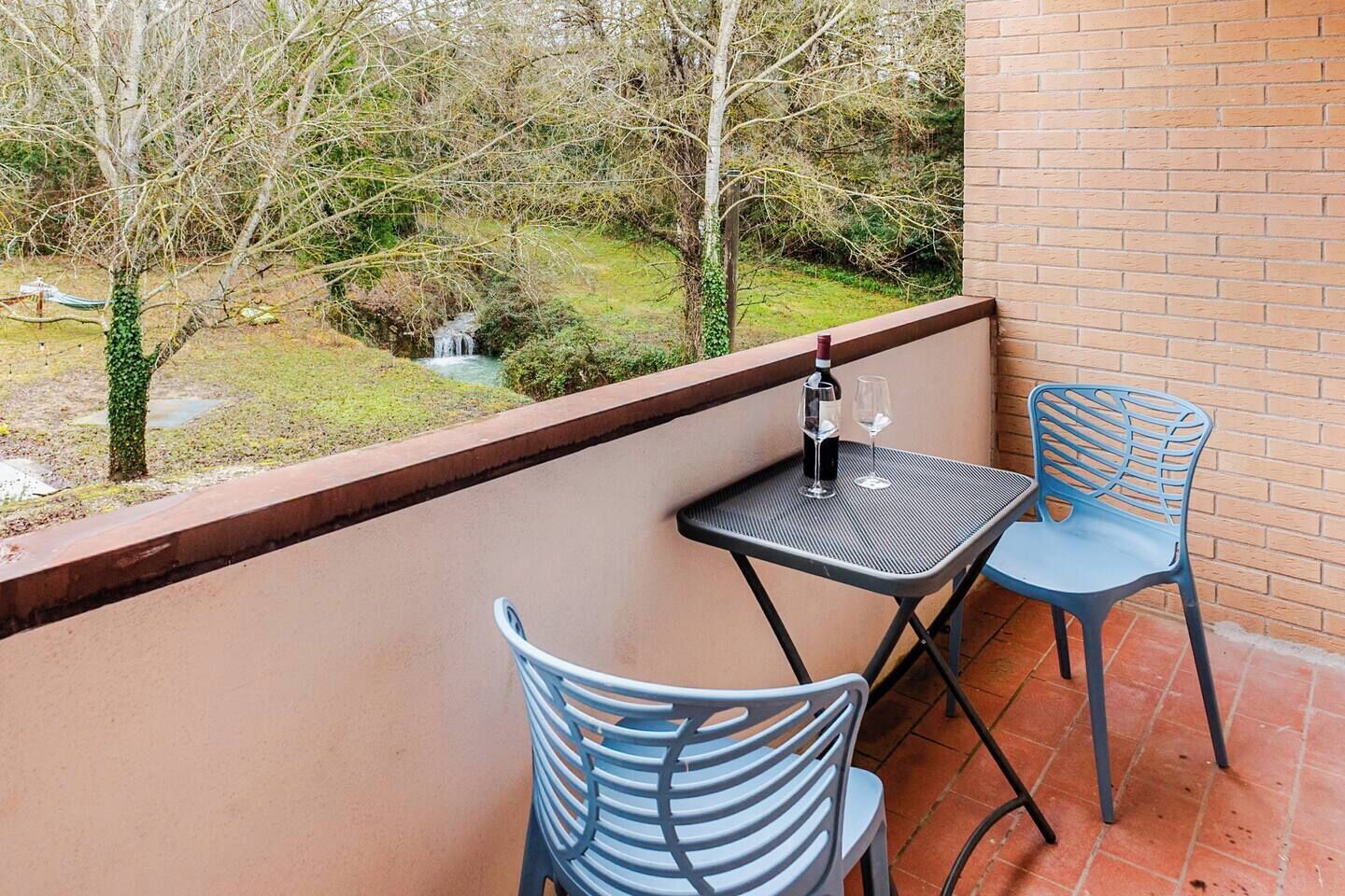 Ein Balkon mit Tisch und zwei Stühlen, der auf einen Garten mit einem kleinen Wasserfall blickt.