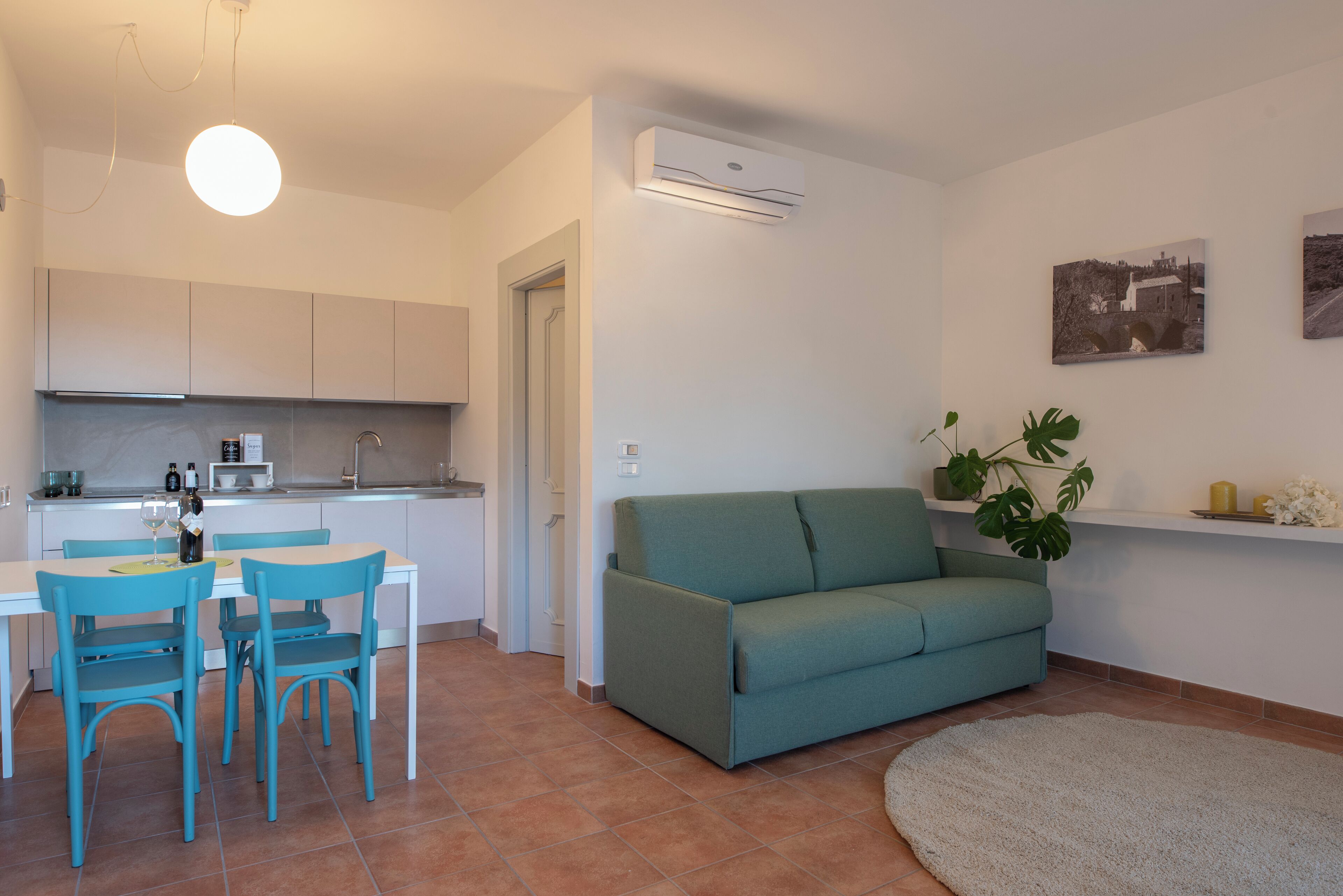 A modern kitchen with white cabinets, a dining table with blue chairs, and a teal sofa in a living area.