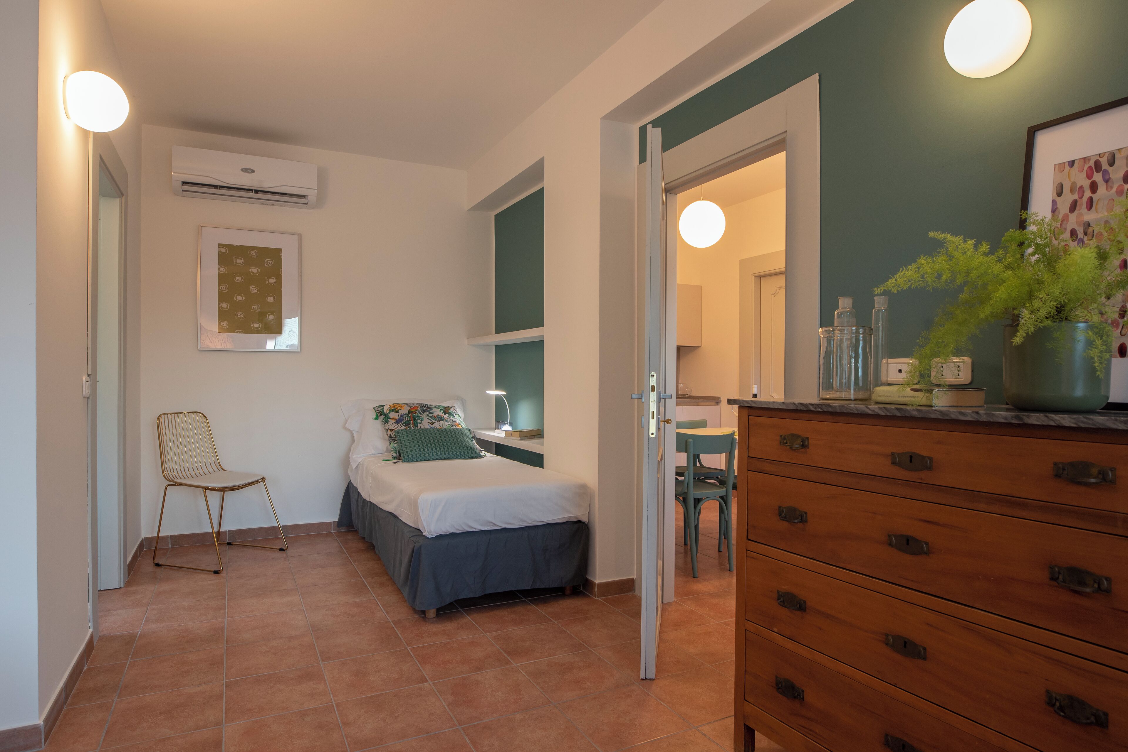 A bedroom with a bed, a chair, a dresser, and an air conditioning unit.
