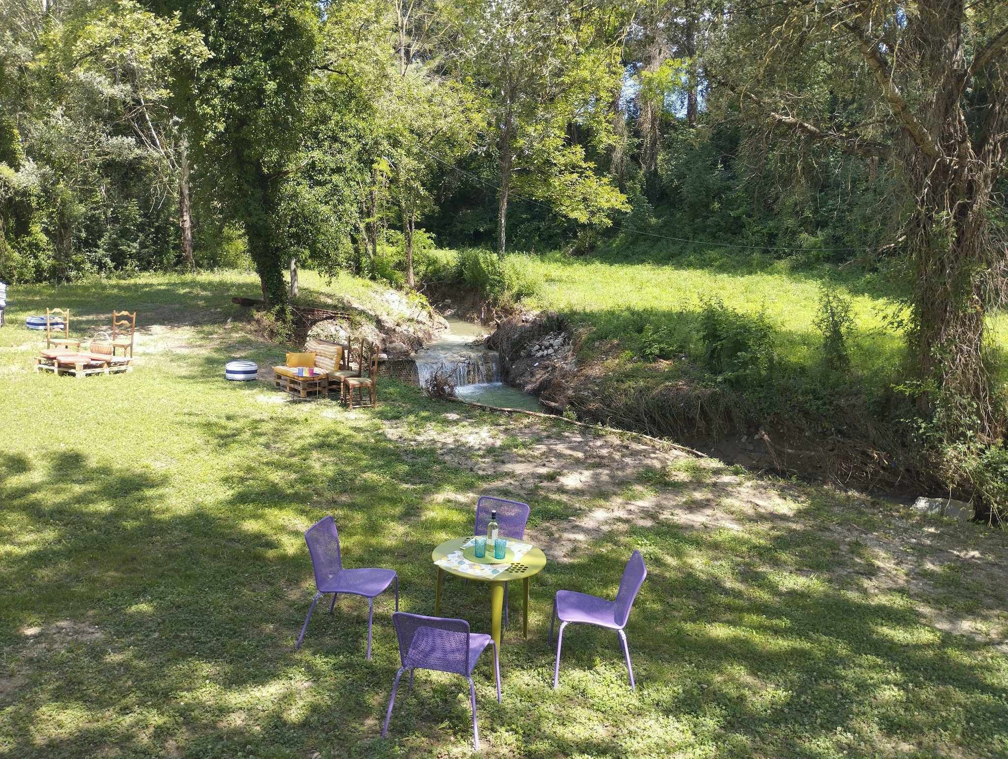 Un espacio al aire libre con césped, un pequeño arroyo, mesas y sillas de picnic.