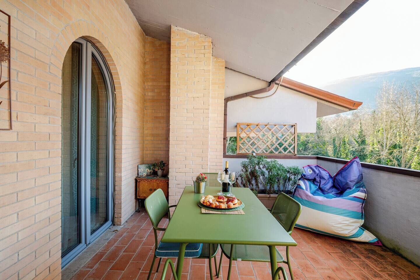 Un balcón con una mesa verde, sillas y un asiento acolchado.