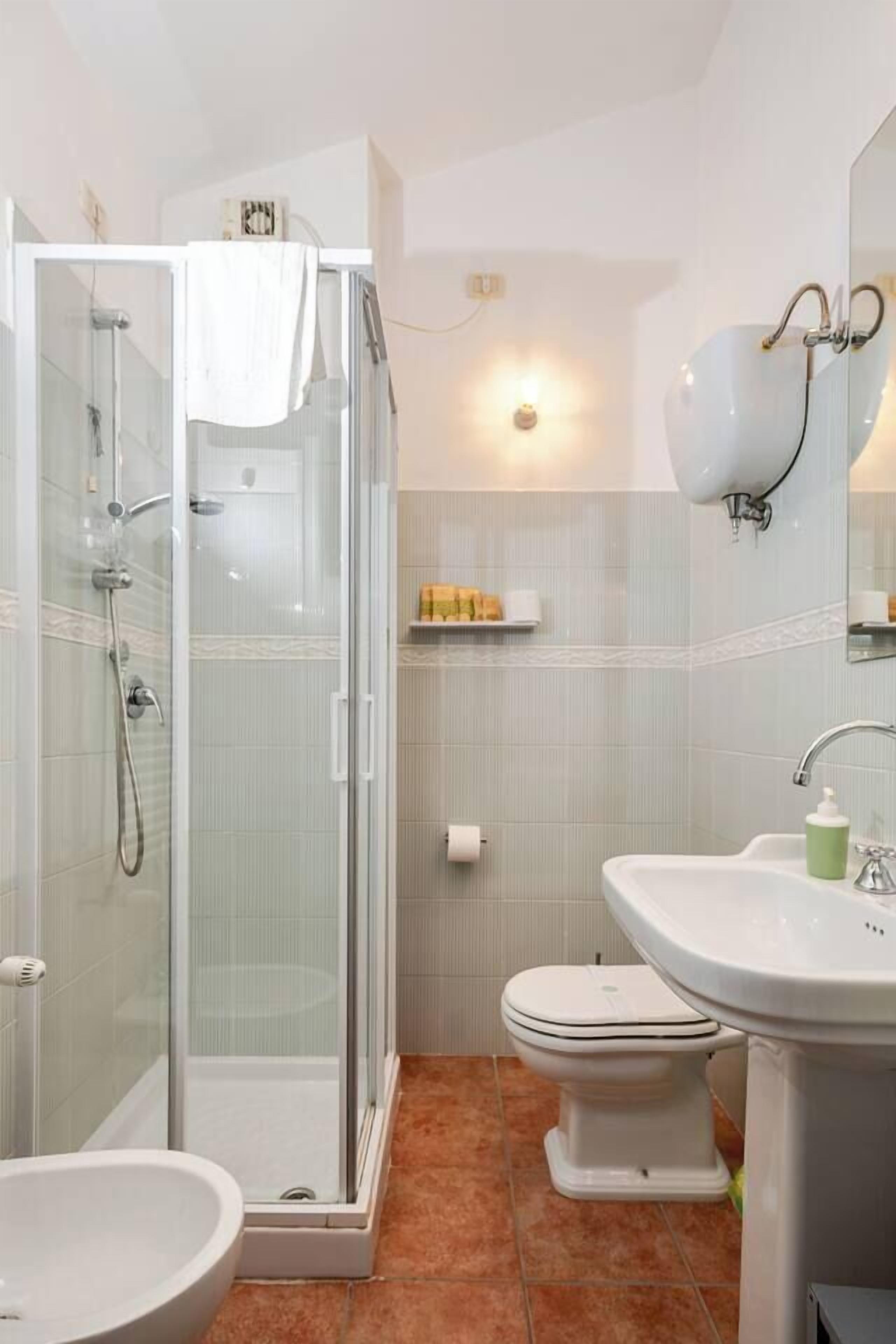 A bathroom with a glass-enclosed shower, a toilet, and a sink.