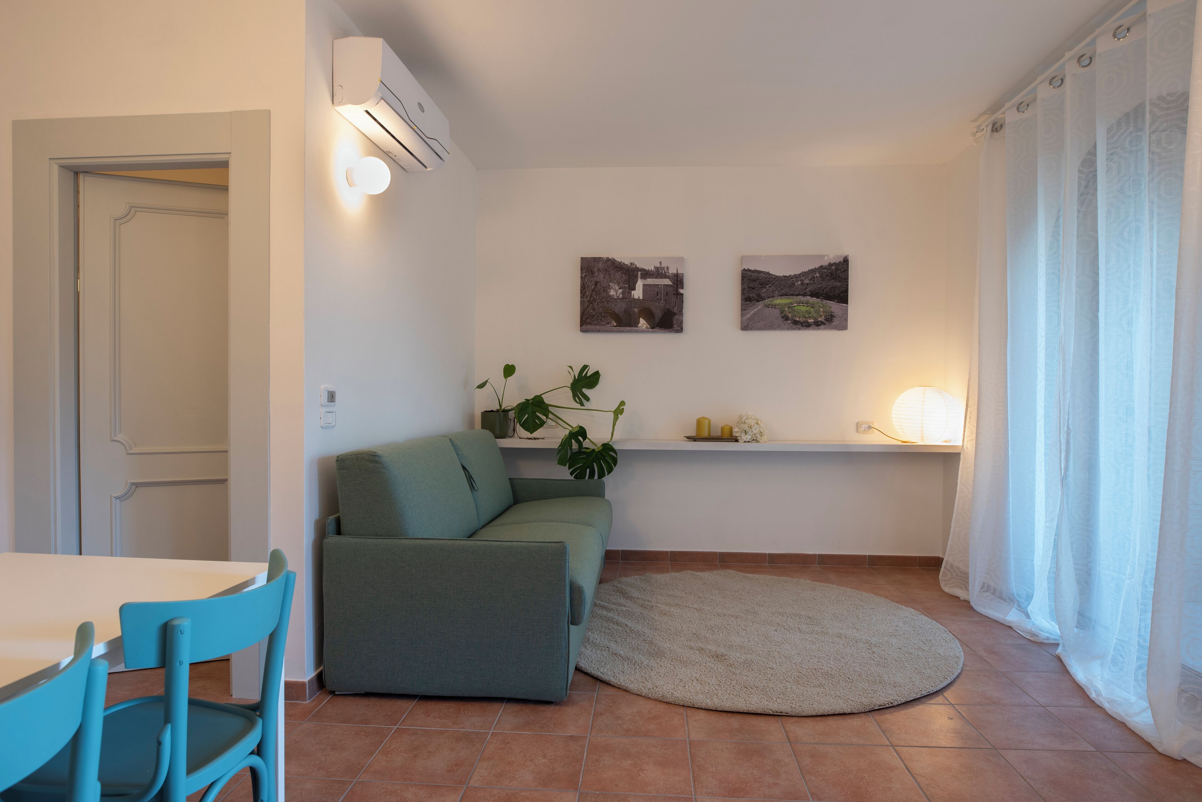 A compact living space with a sofa, a dining table, chairs, a small rug, and two wall-mounted pictures.