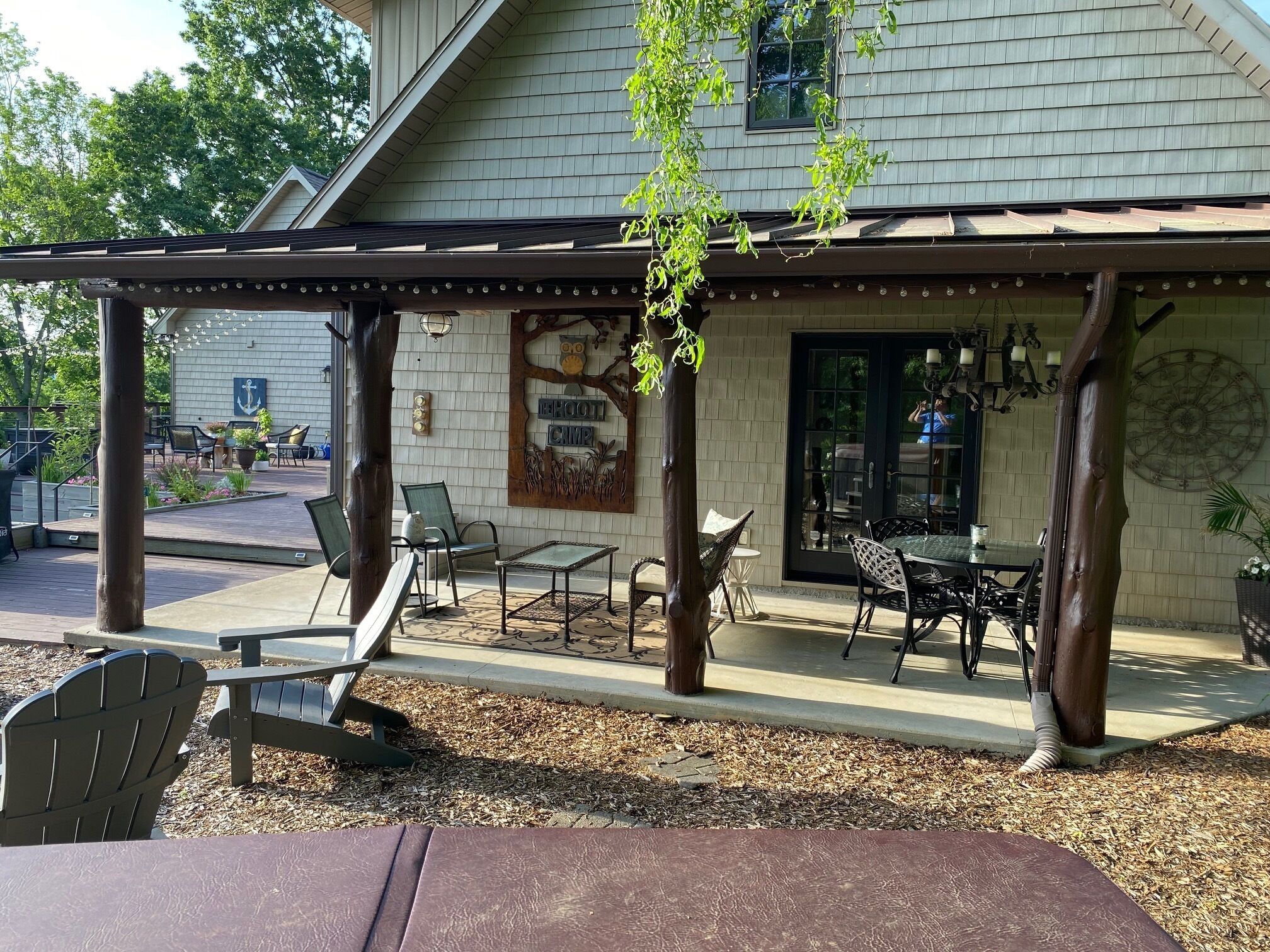 En täckt uteplats med utemöbler, en träpergola och en dekorativ vägg med ett motiv av ett träd och en uggla.