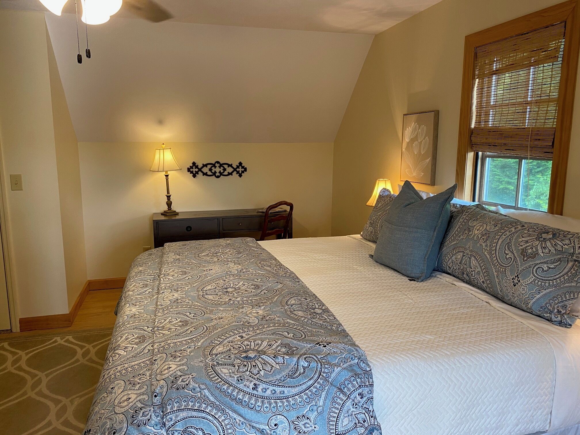 A bedroom with a large bed, two bedside lamps, a wooden nightstand, and a window with blinds.