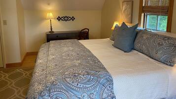 A bedroom with a large bed, two bedside lamps, a wooden nightstand, and a window with blinds.